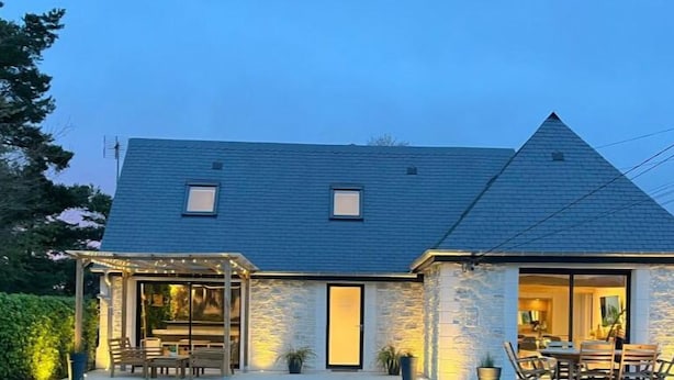 A house with a stone exterior, a sloped roof, and a covered patio area with outdoor furniture.