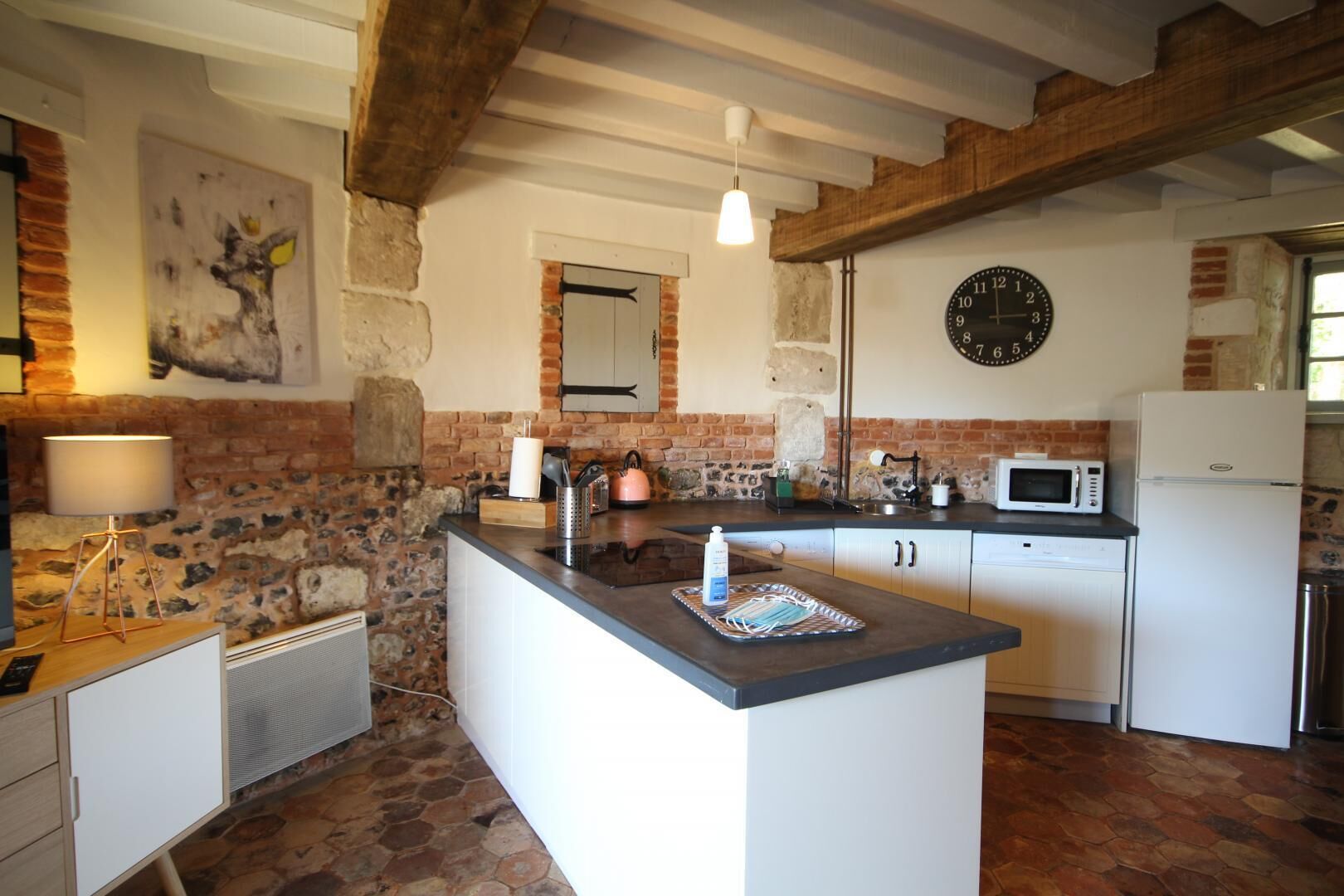 A kitchen with a central island, white cabinetry, a stone wall, a wooden ceiling, a clock, and a microwave.