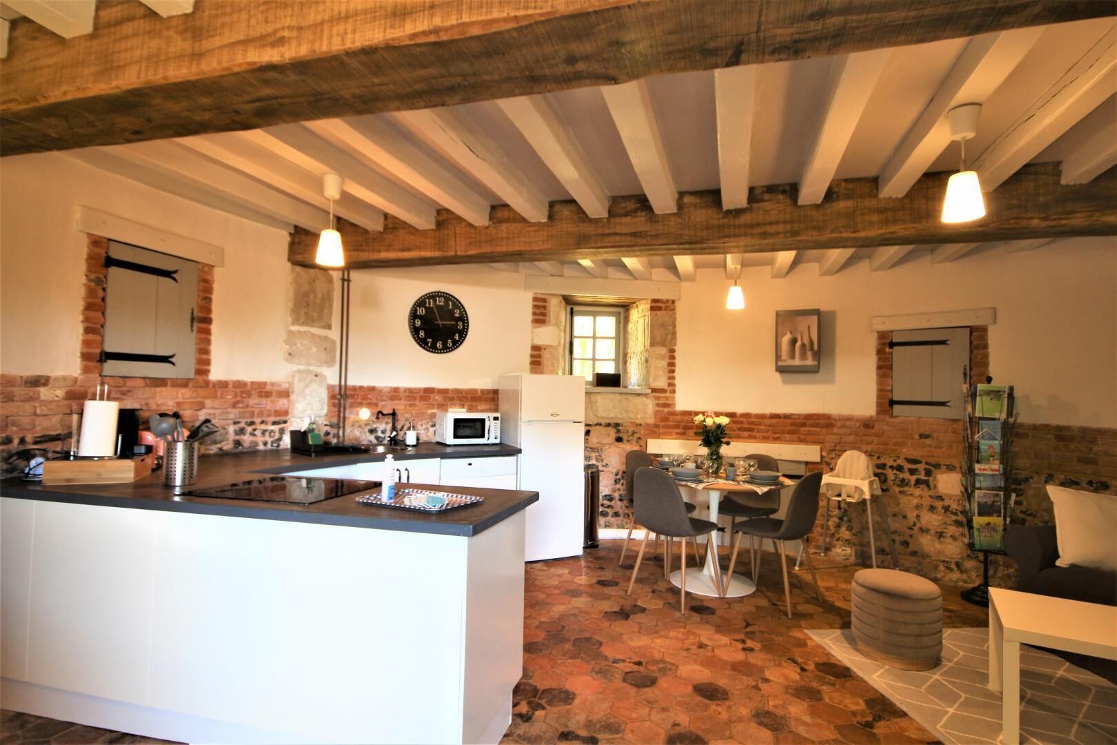 A rustic kitchen with a central island, white cabinetry, exposed brick walls, and a dining area with a table and chairs.