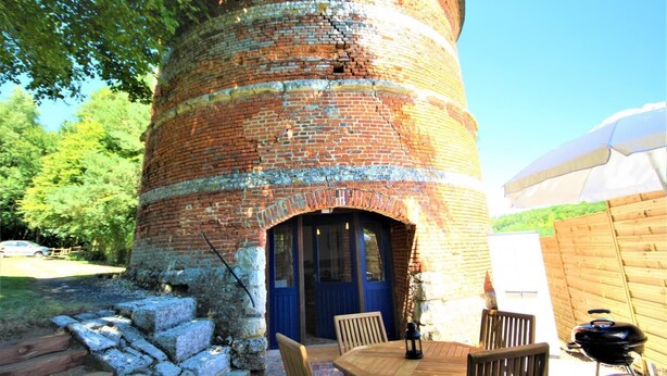 A brick structure with a blue door and a table with chairs outside. - Gîtes de France® - Le Colombier d'Yville (HERONCHELLES)