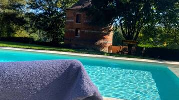 A pool with clear blue water, a brick building in the background, and a purple towel on a chair.