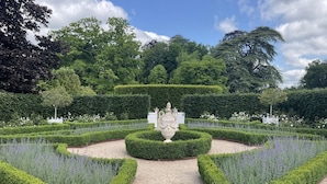A formal garden with a central fountain, neatly trimmed hedges, and a variety of flowering plants. - Gîtes de France® - La Maison Rouge (BOIS HEROULT)