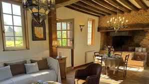 A cozy living room with a sofa, a dining table set for two, and a fireplace. - Gîtes de France® - La Maison Rouge (BOIS HEROULT)