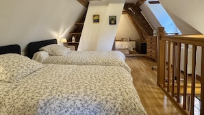 A loft bedroom with two beds, wooden beams, a sloped ceiling, and a wooden railing. - Gîtes de France® - La Maison Rouge (BOIS HEROULT)