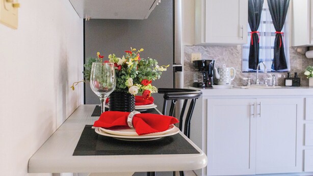Una cocina compacta con armarios blancos, una encimera negra y un comedor con mesa para dos.