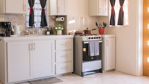 Una cocina con armarios blancos, estufa, lavamanos y una ventana con cortinas.