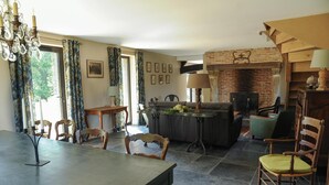 A dining area with a table and chairs, a sofa, a fireplace, and a chandelier. - Gîtes de France® - La Métairie (HANOUARD (LE))