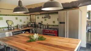 A modern kitchen with a wooden island, stainless steel appliances, and green and white tiled backsplash. - Gîtes de France® - La Métairie (HANOUARD (LE))