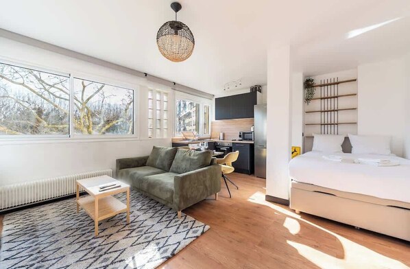 Quarto moderno e bem iluminado com sofá, mesa pequena, cama e cozinha.