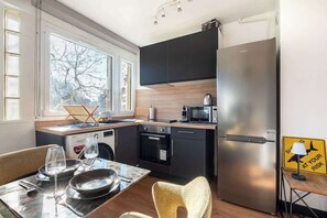 Cozinha compacta com micro-ondas, forno e frigorífico, mesa de jantar posta com pratos e copos, e vista para o exterior através de grandes janelas.