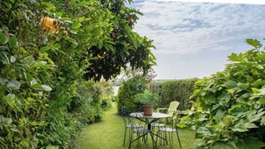 Un jardin avec une table et des chaises, entouré d’une végétation luxuriante et d’une haie.