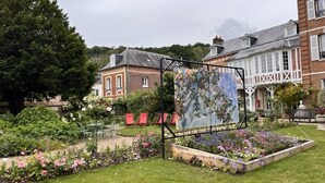 Un jardin agrémenté d’un grand tableau, d’un bâtiment en briques et d’un bâtiment blanc doté d’un balcon.