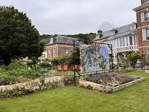 Een tuin met een groot schilderij, een gebouw van baksteen en een wit gebouw met balkon.