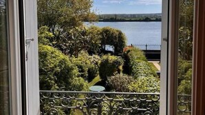 Une vue à travers une fenêtre sur un jardin bien entretenu, avec un lac et un ciel dégagé.