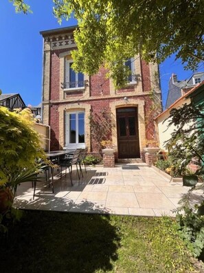 A two-story building with a brick facade, a front door, and a small patio area with a table and chairs.