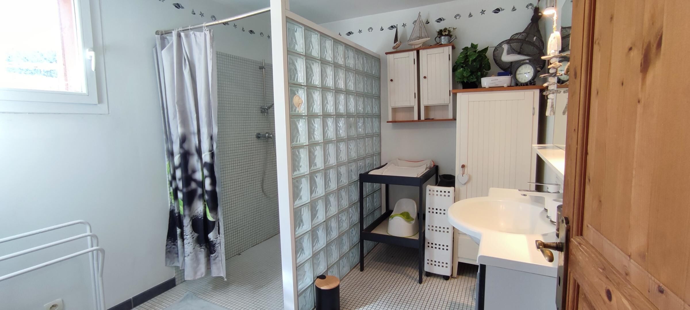 Un baño con ducha, lavamanos, espejo y estante con artículos de aseo.