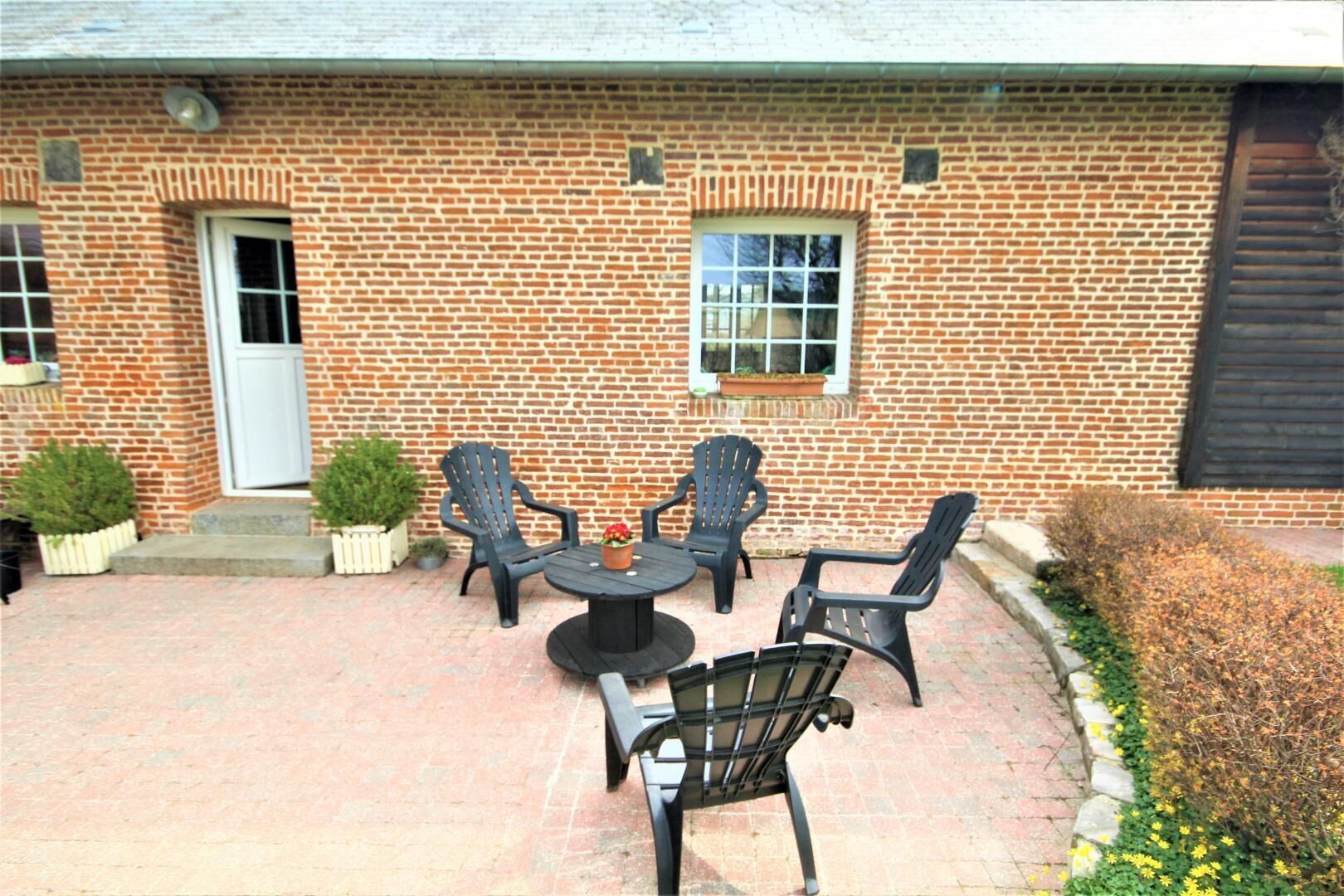 A brick building with a patio area featuring a round table and four Adirondack chairs.