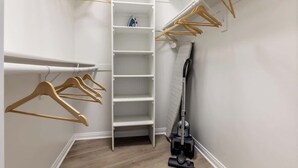 Un vestidor con perchas de madera, un aspirador y una estantería.