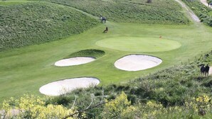 Ein Golfplatz mit Bunkern, einer Fahne und einem Weg.