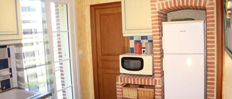 A compact kitchen with a microwave, refrigerator, and a wooden door.
