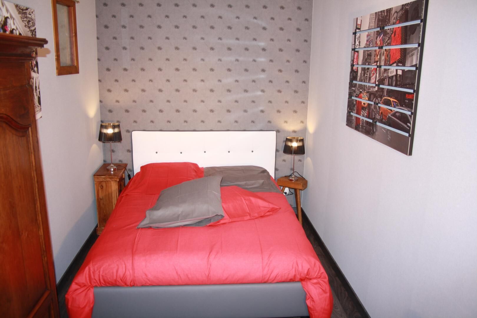 A bedroom with a bed, two bedside tables, a wall with a patterned wallpaper, and a framed picture on the wall.