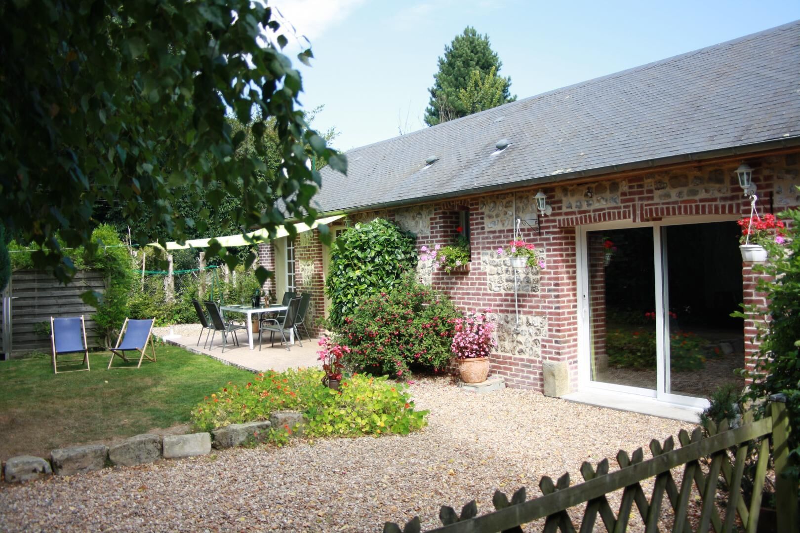 A brick house with a patio, a table with chairs, and a garden with flowers and shrubs.