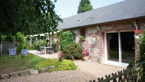 Ein Backsteinhaus mit Terrasse, einem Tisch mit Stühlen und einem Garten mit Blumen und Sträuchern.