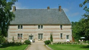 Un bâtiment en pierre de deux étages, doté d’une façade symétrique, d’une entrée centrale et d’une allée de gravier menant à la porte d’entrée.