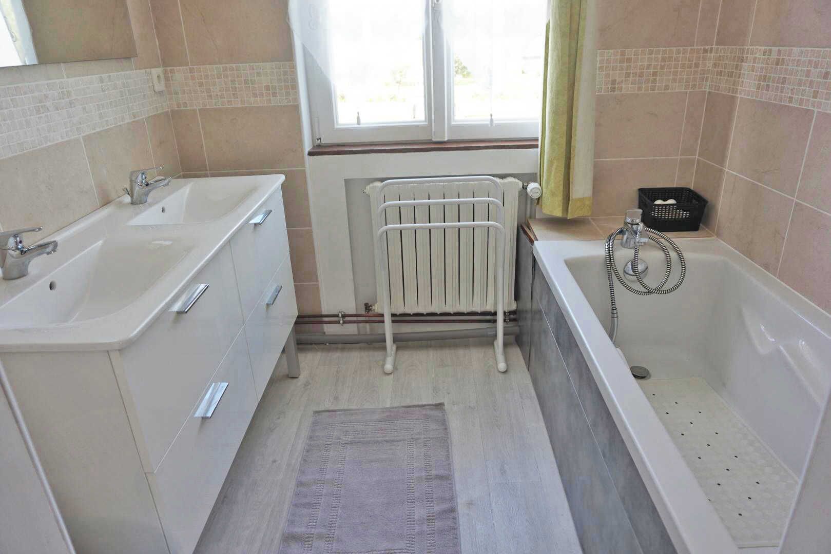 A bathroom with a double sink, a bathtub, a radiator, and a window.
