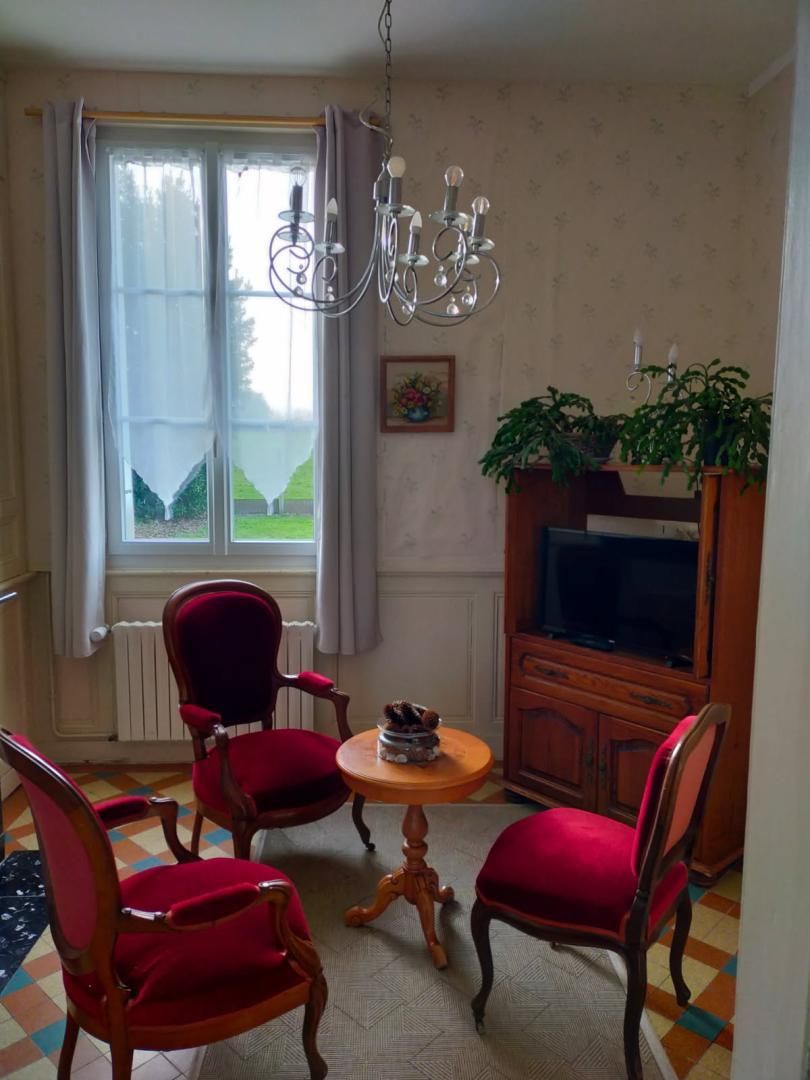 Ein Wohnzimmer mit großem Fenster, einer Kandelaber, einem Fernseher und roten Polstersesseln.