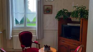 Ein Wohnzimmer mit großem Fenster, einer Kandelaber, einem Fernseher und roten Polstersesseln.