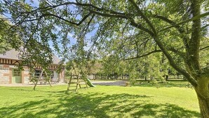 Une cour arrière verdoyante avec une balançoire, un arbre et un bâtiment à la façade en briques.