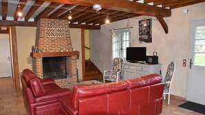 Un salon avec une cheminée en briques, des canapés en cuir rouge, un téléviseur et un escalier menant à un autre niveau.