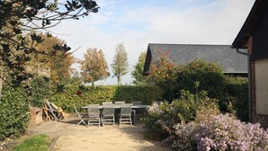 An outdoor patio with a table and chairs, surrounded by a garden with various plants and flowers.