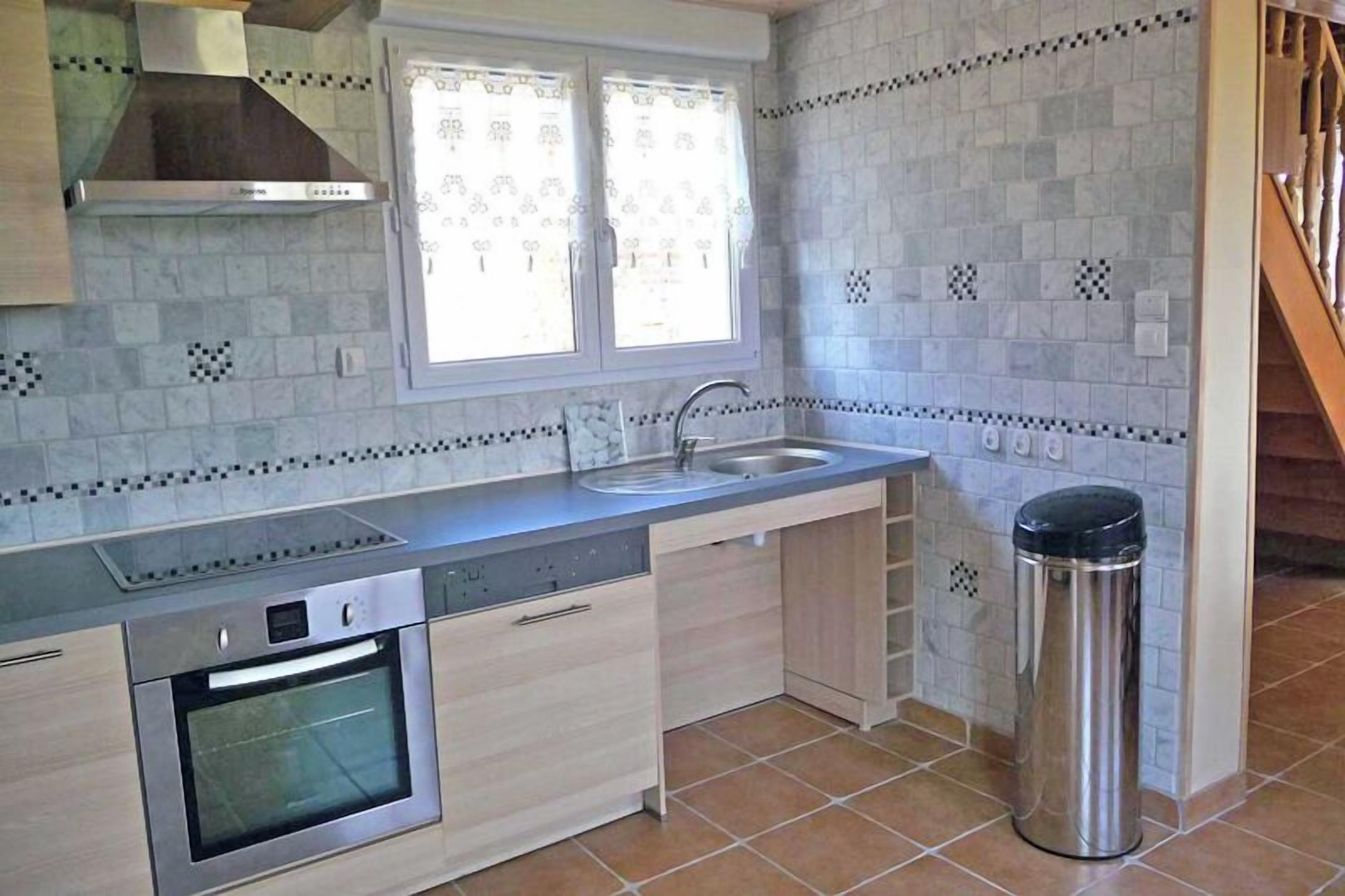 Een kleine keuken met een ingebouwde oven, een roestvrijstalen spoelbak en een raam met patroon gordijnen.