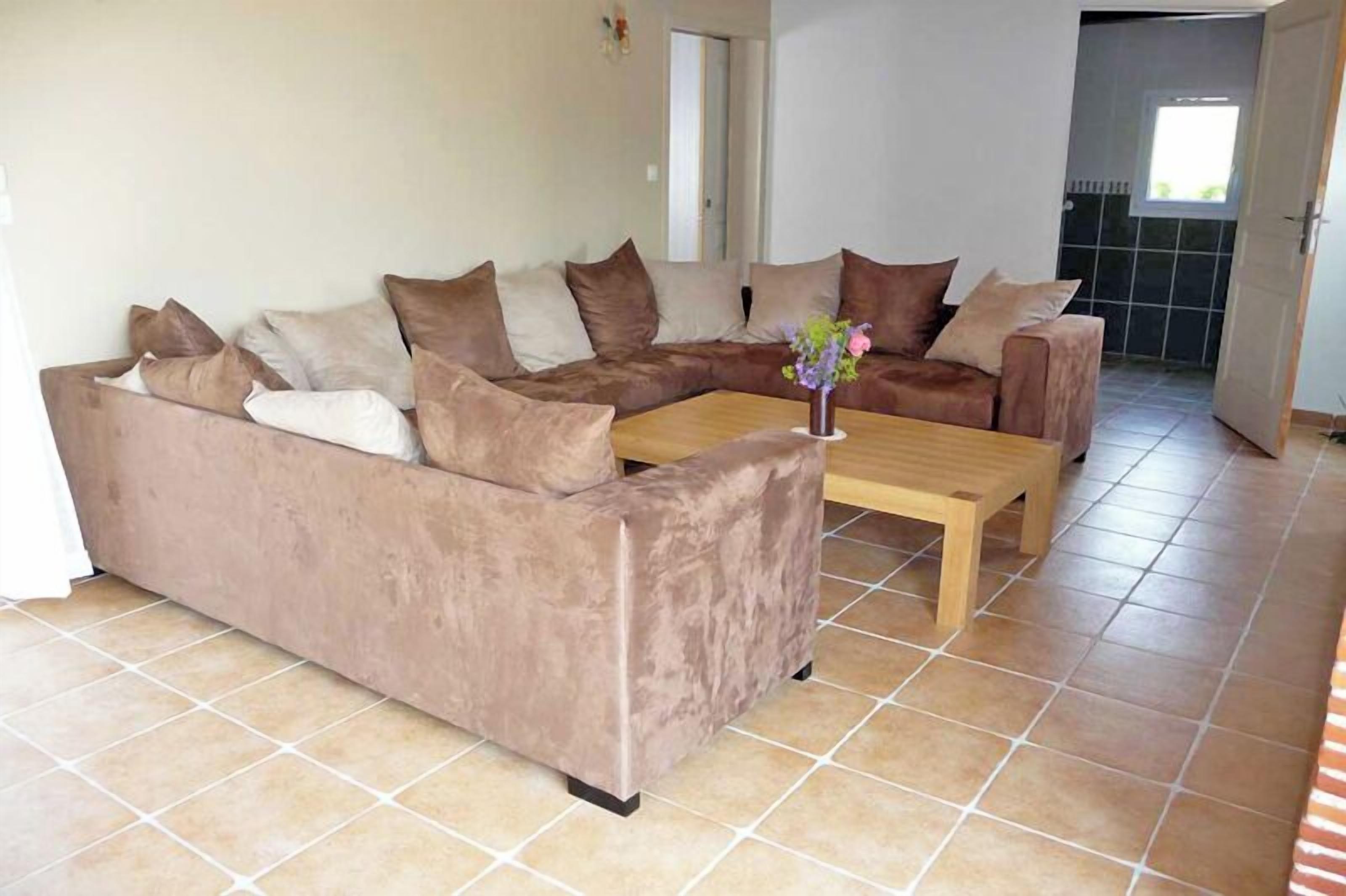 Ein Wohnzimmer mit einem braunen Ecksofa, einem Holztisch und einer Vase mit Blumen.