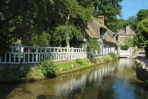 A riverside building with a thatched roof, surrounded by lush greenery and a white fence. - Gîtes de France® - Le Rançon (TOUFFREVILLE LA CORBELINE)