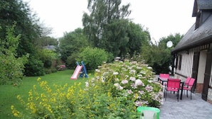 Ein Garten mit Spielbereich, einer Terrasse mit Stühlen und einem Gebäude mit Satteldach.