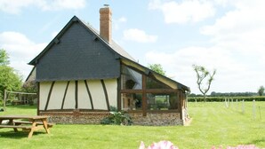 Une maison traditionnelle à colombages, avec une cheminée, une grande fenêtre et un banc en bois au premier plan.