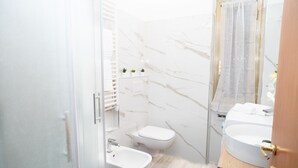 A compact bathroom with a white marble wall, a wooden vanity, a white sink, a bidet, and a toilet. - Minimal and Functional: Stay Near the Vatican (Roma)