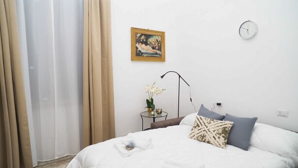 A bedroom with a bed, a nightstand, a clock, and a painting on the wall. - Minimal and Functional: Stay Near the Vatican (Roma)