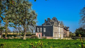 Une grande maison historique, reconnaissable à sa façade noire imposante, à ses nombreux conduits de cheminée et à son jardin bien entretenu.