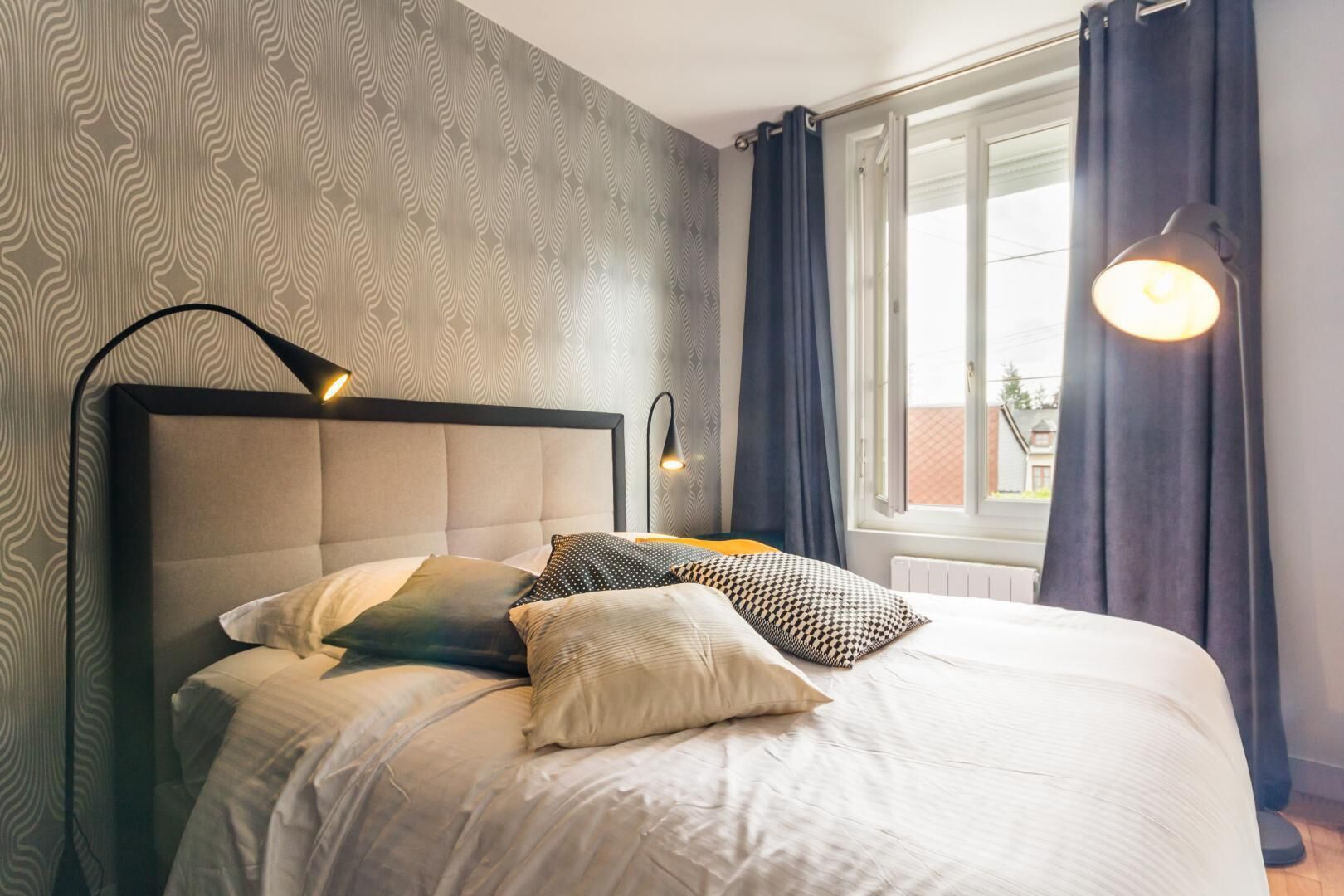 A neatly made bed with a headboard, multiple pillows, and a bedside lamp.