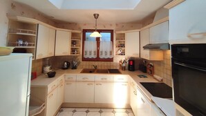 A compact kitchen with a skylight, white cabinets, a black stove, and a window with curtains.