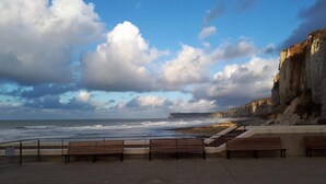 A coastal promenade with benches and a view of the sea and cliffs.