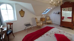 A bedroom with a large bed, a wooden wardrobe, a chandelier, a desk, and a window with a view.