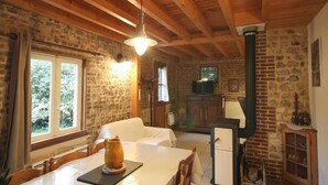 Una habitación rústica con pared de piedra, vigas de madera, chimenea, televisor y una mesa con una jarras.