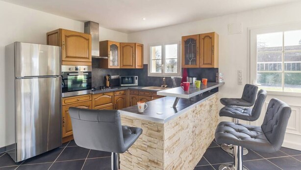 A modern kitchen with a central island, stainless steel appliances, wooden cabinets, and a large window.