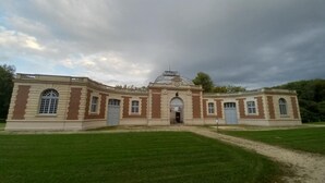 Un grand bâtiment historique doté d’un dôme central et d’une architecture symétrique, entouré de pelouses bien entretenues.