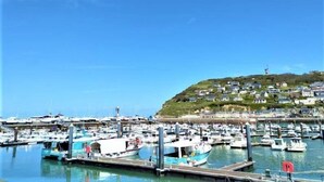 Un port de plaisance où sont amarrés de nombreux bateaux, un ciel bleu dégagé et une colline avec des bâtiments en arrière-plan.